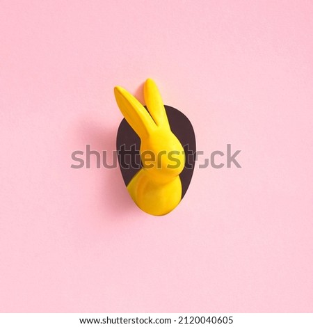 Yellow Easter bunny looks out of an egg-shaped hole in the pink background wall. Abstract concept. Square with copy space. Royalty-Free Stock Photo #2120040605