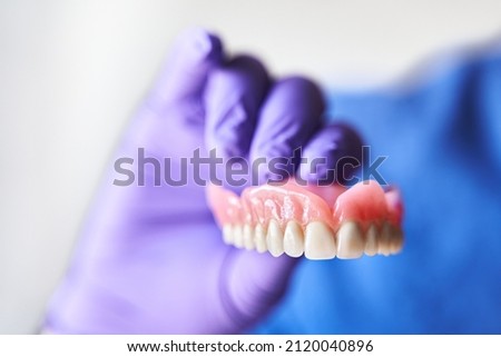 Dentist with purple gloves holding dentures in hand. Concept of dental prosthesis and dental health. Royalty-Free Stock Photo #2120040896