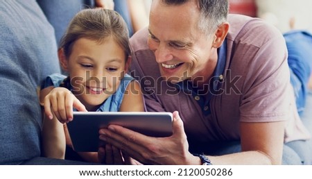 Modern day family time. Shot of a cute little girl using a digital tablet with her father on the sofa at home.