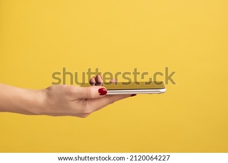 Closeup portrait of smartphone flat lying on open woman palm, female giving mobile phone. Indoor studio shot isolated on yellow background. Royalty-Free Stock Photo #2120064227