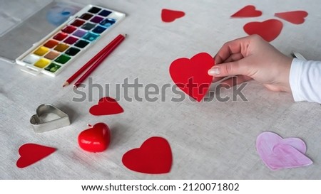Hand holds red paper heart on table background. Preparation for St. Valentine's day 14 february: red hearts, greeting card