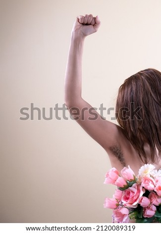 Strong woman holding a flowers in her hand, show her natural body female hairy armpit, fashion trend concept power feminism, unshaven underarms on yellow background.