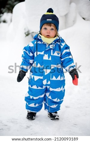 Beauty baby girl in blue and white snowsuit and r hat playing outside in snow on beauty winter day Royalty-Free Stock Photo #2120093189