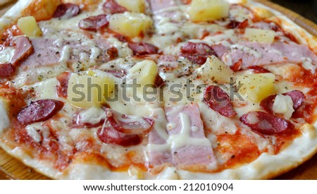 Round pizza with sausages and pineapple on a wooden plate