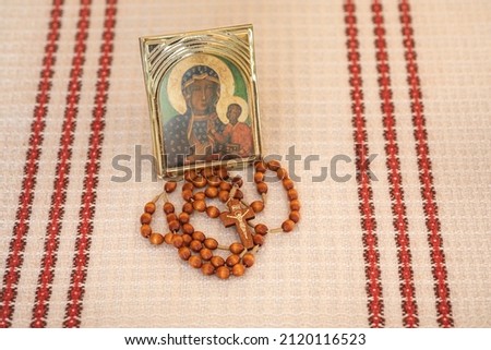 Rosary, icon of Our Lady and a cross on a light brown background.