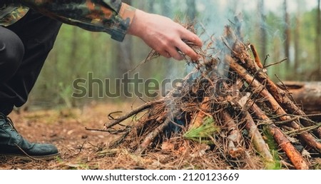 Low angle shot of a man is trying make a fire in the forest. Close-up of a man's hand lighting a campfire. Lighting a fire in the forest by a person. Low angle of a burning fire made of brushwood. Royalty-Free Stock Photo #2120123669