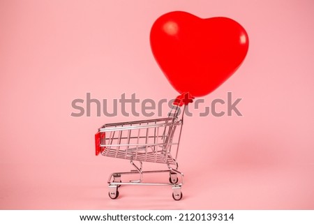 Valentine's day. Shopping cart with an inflated balloon in the shape of a heart on a pink background. The concept of holiday shopping.