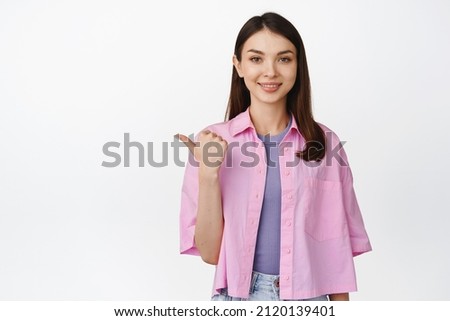 Image of smiling caucasian girl pointing left, looking at camera, recommending store sale, standing over white background