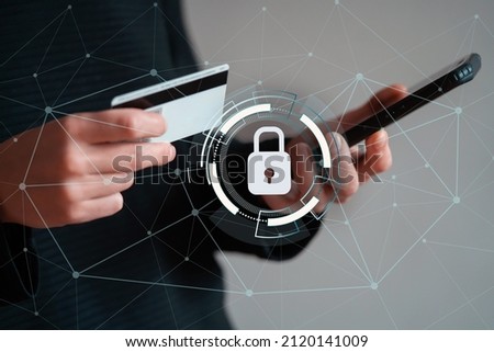 Hands hold a bank card and a mobile phone, person takes care of the security of the account and finances, passes verification, close up view. Symbols of security, a lock in a circle are added.