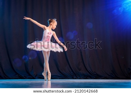 A little girl ballerina is dancing on stage in a white tutu on pointe shoes a classic variation. Royalty-Free Stock Photo #2120142668