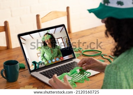 Caucasian woman holding shamrock glasses while having a video call on laptop at home. st patricks celebration concept