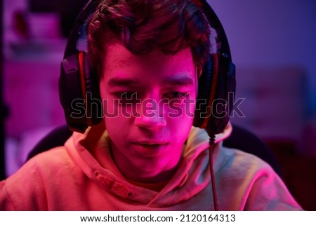 Portrait of teenager boy playing computer video game in dark room, workplace for cybersport gaming, children gaming addiction