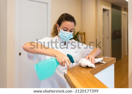 Cleaning lady using a face mask while cleaning the reception desk of a Spa or health center.