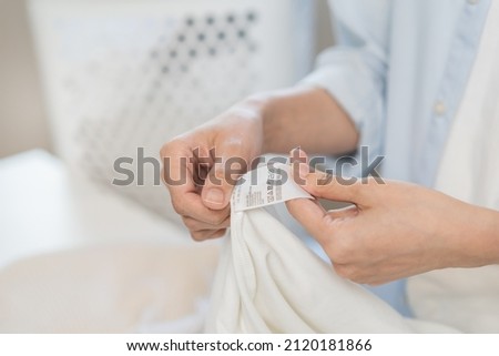 Housewife, asian young woman hand in holding shirt label, tag with instructions, guide before clean clothes, fabric into washing, drying machine, making household working at home. Laundry and maid. Royalty-Free Stock Photo #2120181866