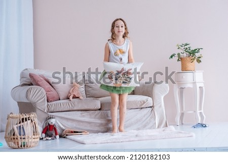 A cute little girl with dark curly hair in a puffy green skirt plays with toys in the children's room. A child with a pillow in his hands. Studio photo.