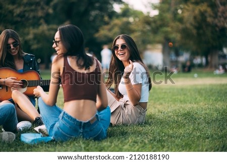 Beautiful and attractive girl friends are smiling and laughing while sitting on the grass Royalty-Free Stock Photo #2120188190