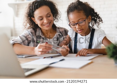African-american mom mother tutor nanny childminder drawing together helping assisting with homework school project to a preteen daughter. Homeschool concept. E-learning on laptop Royalty-Free Stock Photo #2120194271