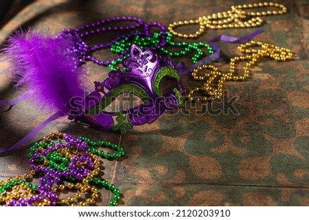 Colorful festive mardi gras or carnivale mask with green, violet and yellow beads on a rustic tile background, selective focus, copyspace