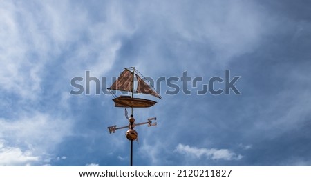 Vintage weather vane in the form of ship on the background with blue dark sky and white clouds, Bulgaria