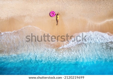 Aerial view of the lying beautiful young woman with pink swim ring on the sandy beach near sea with waves at sunset. Summer vacation in Lefkada island, Greece. Top view of slim girl, clear azure water Royalty-Free Stock Photo #2120219699