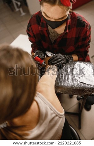 Professional tattoo master making tattoo on client body wering gloves and protective mask