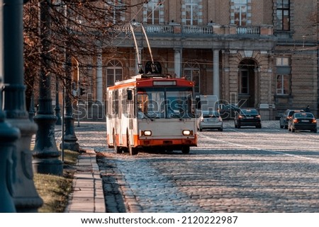 Old red and white trolleybus rides along a paved sidewalk in the center of a European city (1149) Royalty-Free Stock Photo #2120222987