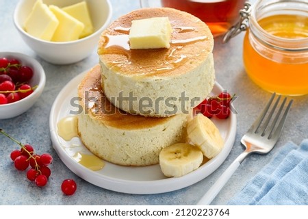 Fluffy Japanese Souffle pancakes with honey, red currants and banana on a white plate. Asian dessert for breakfast. Selective focus Royalty-Free Stock Photo #2120223764