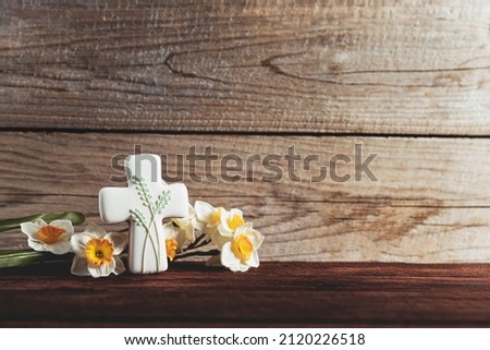 Easter holiday conceptual background on rustic wooden boards. Photo of gingerbread cookie Cross shape, narcissus or daffodils flowers on table top. Card with copy space to place text. Minimal concept Royalty-Free Stock Photo #2120226518