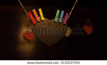 wooden heart hanging from a rope and gripped with tweezers with LGBT colors