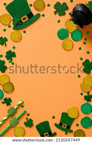 St Patrick's Day vertical banner design. Irish leprechaun hats, pot of gold, and shamrock clover leaves on orange background with copy space. Happy Saint Patricks Day concept. Flat lay, top view.