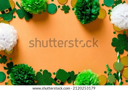 Happy St Patricks Day card design. Frame made of shamrock clover leaves, gold coins, green decorations on orange background. Flat lay, top view. Vintage style.