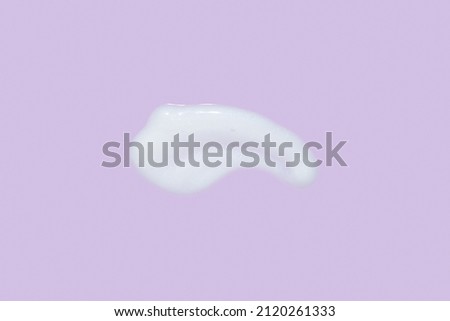 The texture of a facial skin care product. Smears of white cream with shimmer effect on a lilac background. Anti-aging anti-wrinkle care