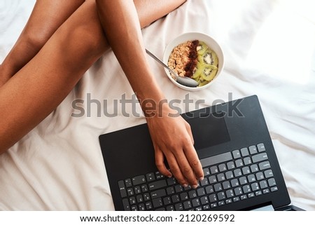 I got this breakfast idea online. Cropped shot of an unrecognizable woman sitting on her bed with her laptop and a bowl of oats.