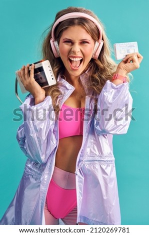 This mixtape always get everyone jamming. Studio shot of a young woman holding a cassette player while dressed in 80s clothing. Royalty-Free Stock Photo #2120269781