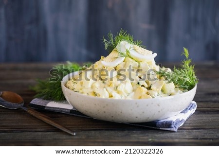 Bowl of egg salad sandwich spread with fresh boiled eggs and dill over a rustic wood table. Selective focus with blurred foreground and background.