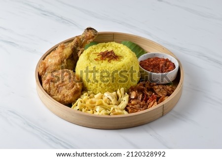 Nasi Kuning or yellow rice, Indonesian turmeric rice with assorted side dishes such as scrambled tempeh, sliced omelet, fried chicken, chili paste, mashed potato fritters, and shrimp crisp Royalty-Free Stock Photo #2120328992