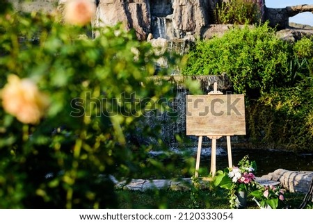Welcoming wedding guests in a beautiful green garden. Empty Wooden wedding sign with colors roses decorations
