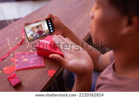 Biracial young man with bouquet during online dating with boyfriend blowing kiss on valentine day. unaltered, online dating, video call, lgbtqi and distant valentine day celebration.