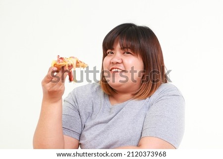 Fat Asian woman holding pizza She is happy to eat. The concept of choosing foods that are beneficial to the body. White background. Royalty-Free Stock Photo #2120373968