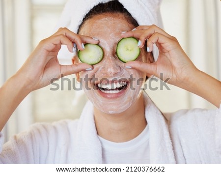 I needed a spa day. Shot of a beautiful young woman holding cucumbers in front of her eye during her beauty routine. Royalty-Free Stock Photo #2120376662