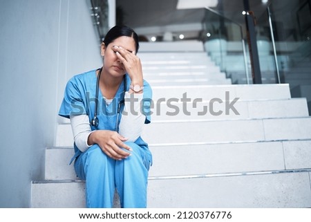 Sometimes not everything is in our hands. Shot of a female nurse looking stressed while sitting on a staircase. Royalty-Free Stock Photo #2120376776