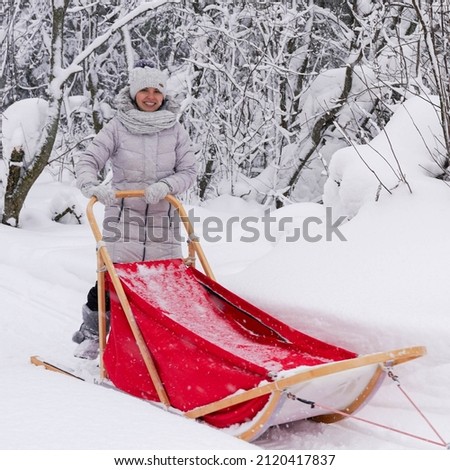 Musher woman hiding behind sled at dog race on snow in winter.