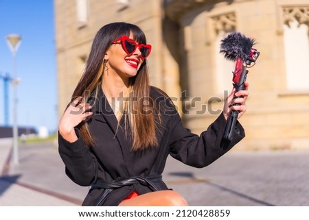 Brunette caucasian girl making a vlog on Valentine's day, red heart sunglasses, talking on the phone and microphone