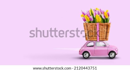 Pink toy car delivering flowers tulips in a wicker basket on a pink background. Valentine day, flowers delivery, womens day. Place for text. Royalty-Free Stock Photo #2120443751