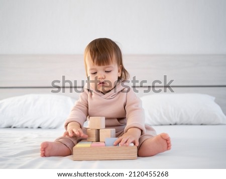 Happy preschool child girl sitting on the bed plays an educational game with blocks. Eco-friendly toys for children without plastic. Banner. copy space.