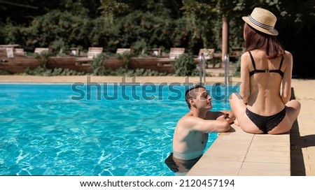 Young adult woman sitting on the edge of the pool laughing and flirting with a man floating in the water. The concept of romance and flirting while on vacation at the resort. copy space. Royalty-Free Stock Photo #2120457194