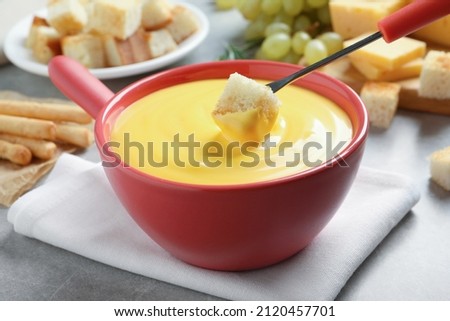 Dipping piece of bread into tasty cheese fondue at grey table