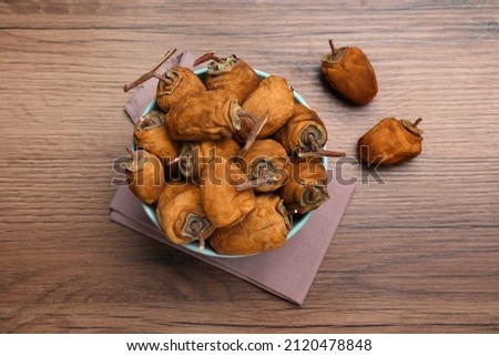 Bowl with tasty dried persimmon fruits on wooden table, flat lay