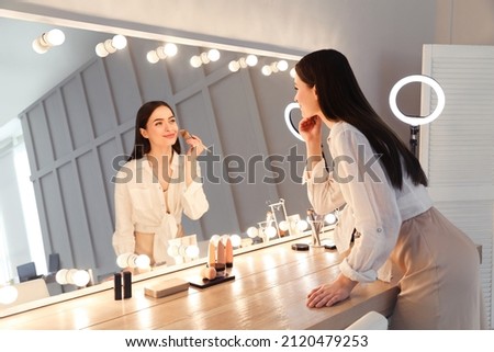 Young woman applying make up near illuminated mirror indoors Royalty-Free Stock Photo #2120479253