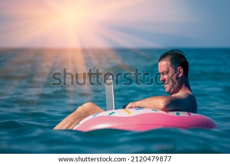 Working anywhere and any time. Businessman working, using laptop computer on inflatable ring in the water.